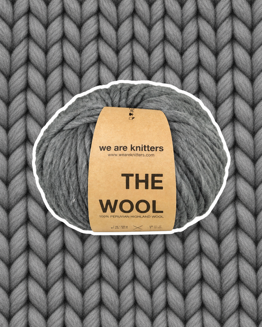 The Wool Spotted Dark Grey yarn ball on a matching knit swatch